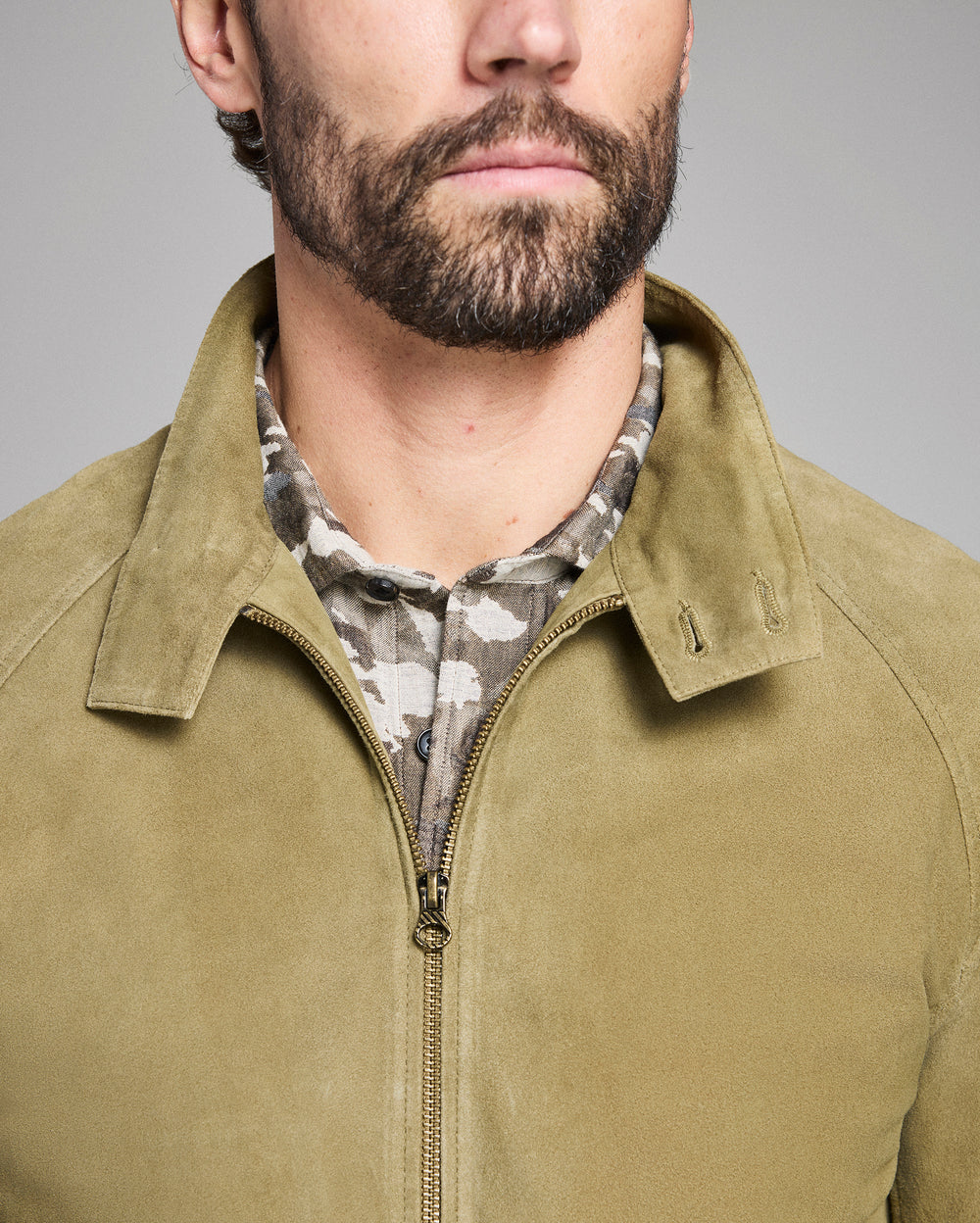 Man wearing a green jacket with a camouflage shirt underneath on a gray background