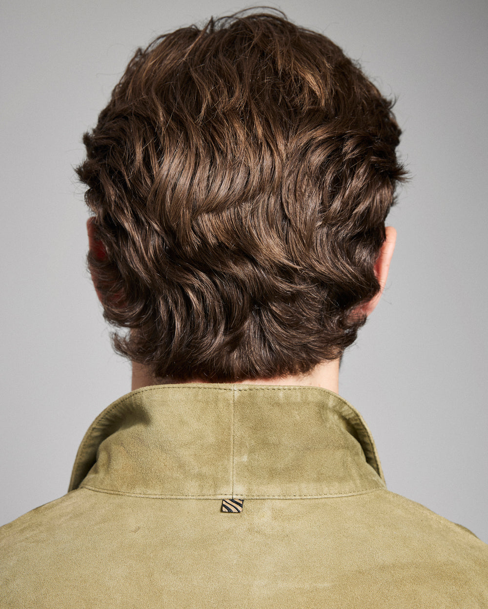 Back view of a person with styled hair wearing a green shirt against a gray background
