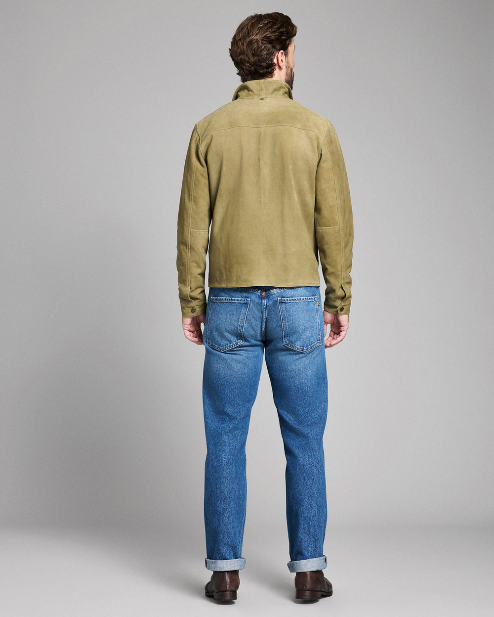 Man wearing a green jacket and blue jeans on a gray background