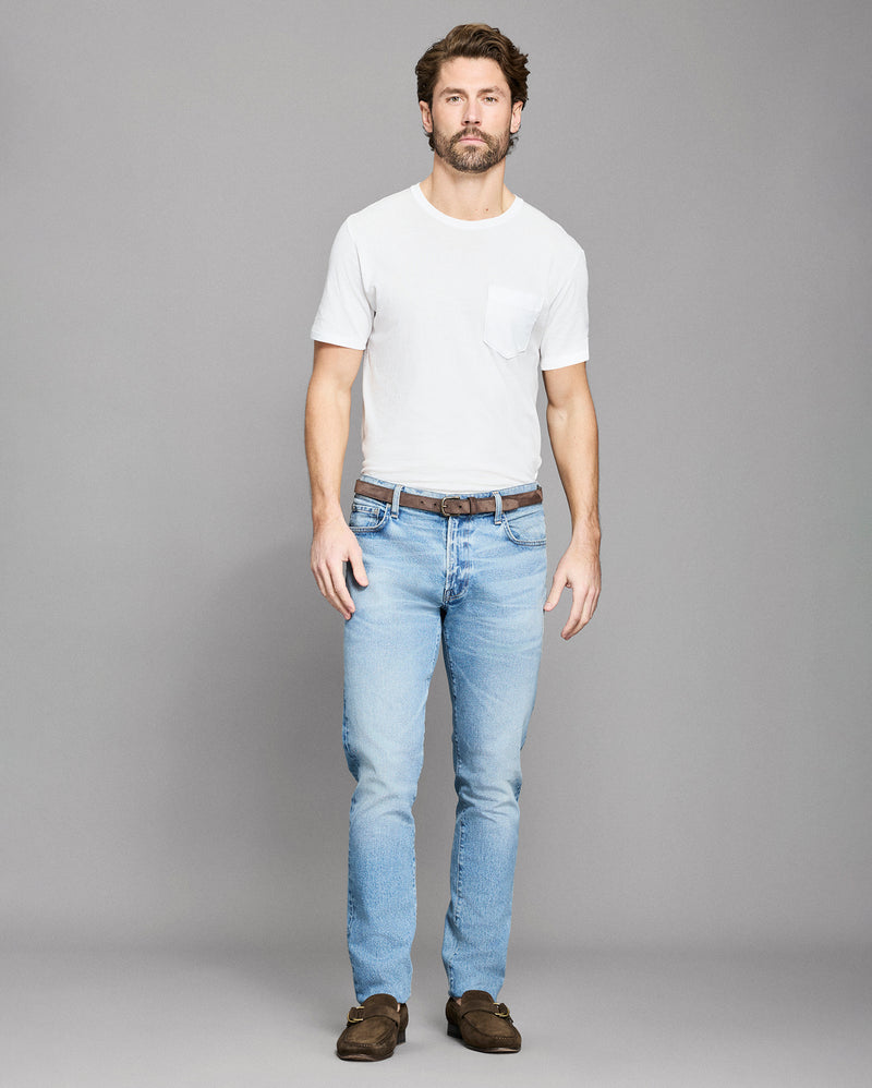 Man wearing a white t-shirt and light blue jeans on a gray background Alternate