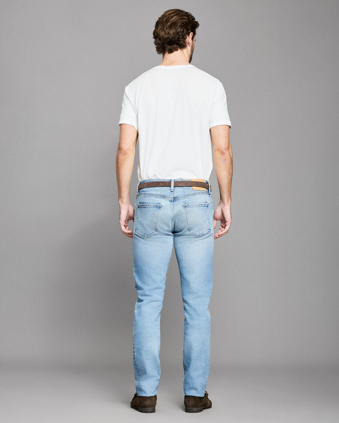 Man wearing light blue jeans and a white t-shirt on a gray background