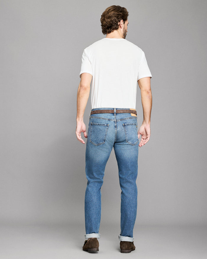 Man wearing blue jeans and a white t-shirt on a gray background