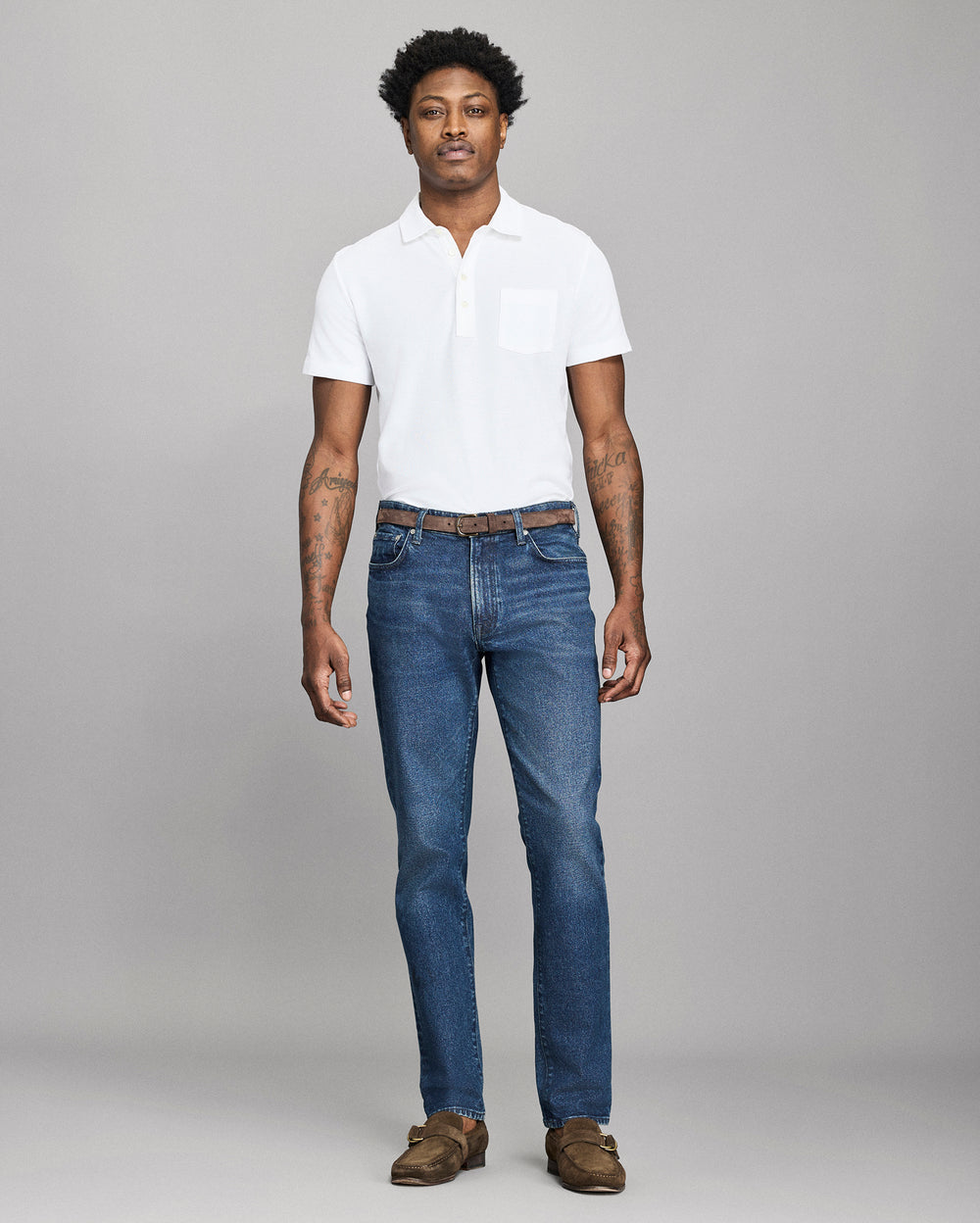 Man wearing a white polo shirt and blue jeans against a gray background