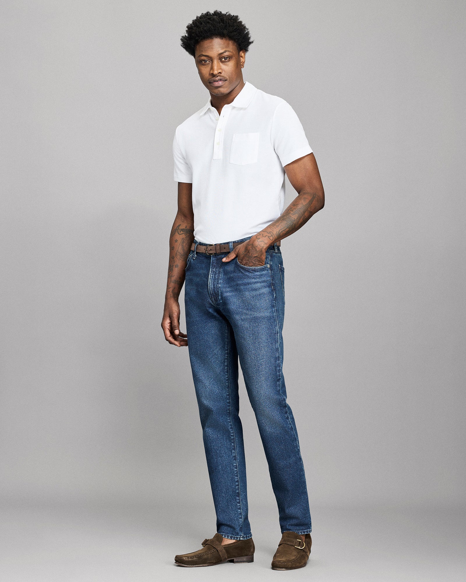 Man wearing a white polo shirt and blue jeans against a gray background