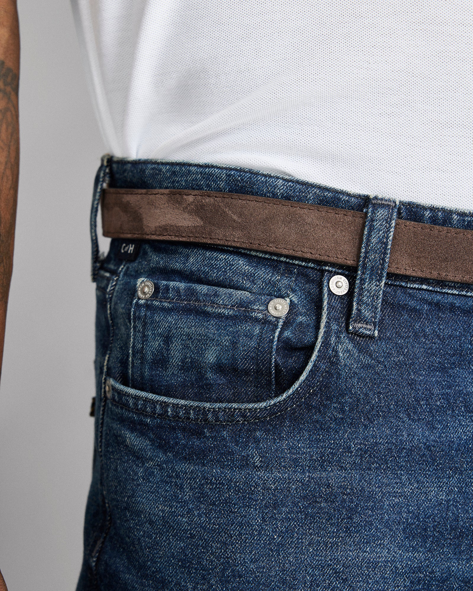 Close-up of blue jeans with a brown belt on a gray background