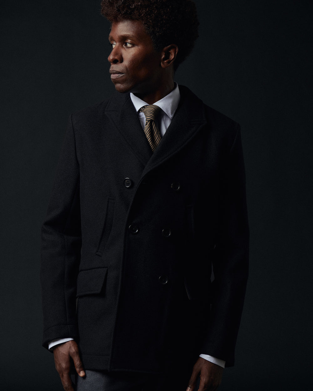 Man wearing a dark coat and tie against a black background