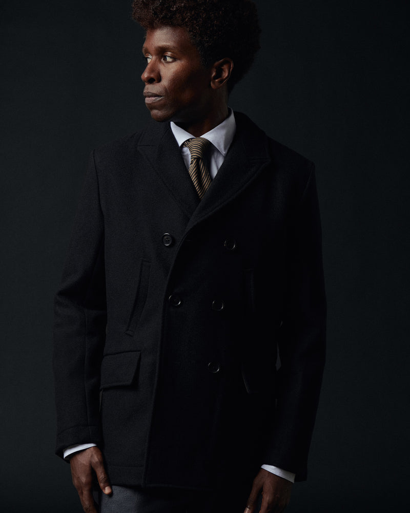 Man wearing a dark coat and tie against a black background Alternate