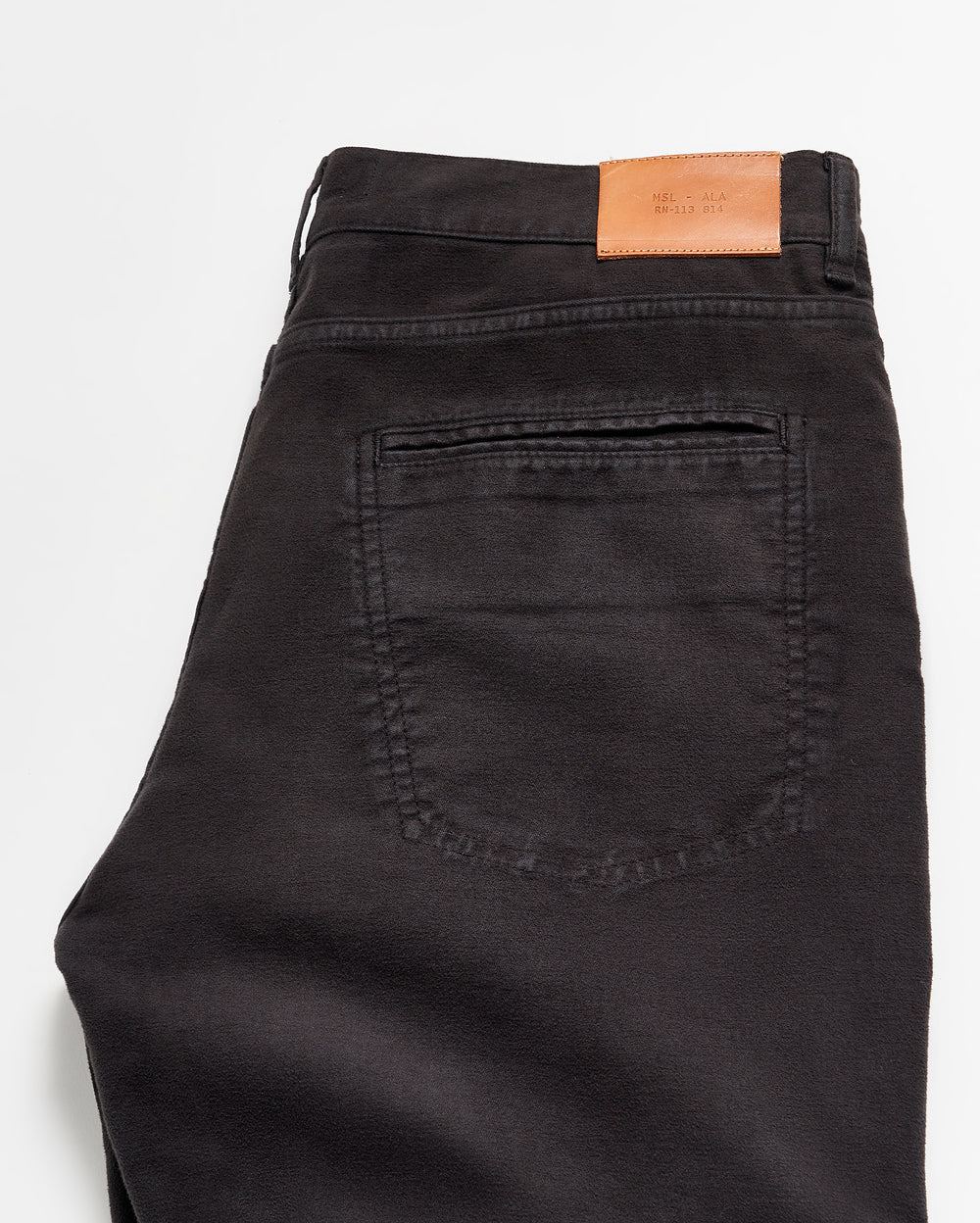 A pair of black jeans folded neatly, showing the back pocket and a brown leather patch on the waistband with small printed text.