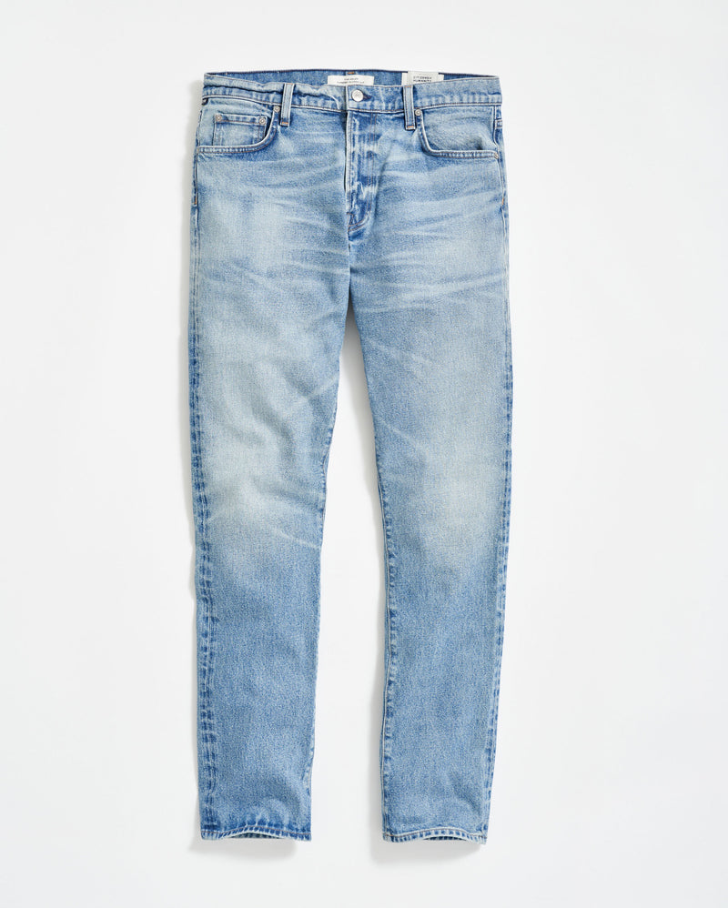 A pair of light blue, slim-fit jeans with a slight faded and worn effect, five pockets, and button fly, displayed flat on a white background.