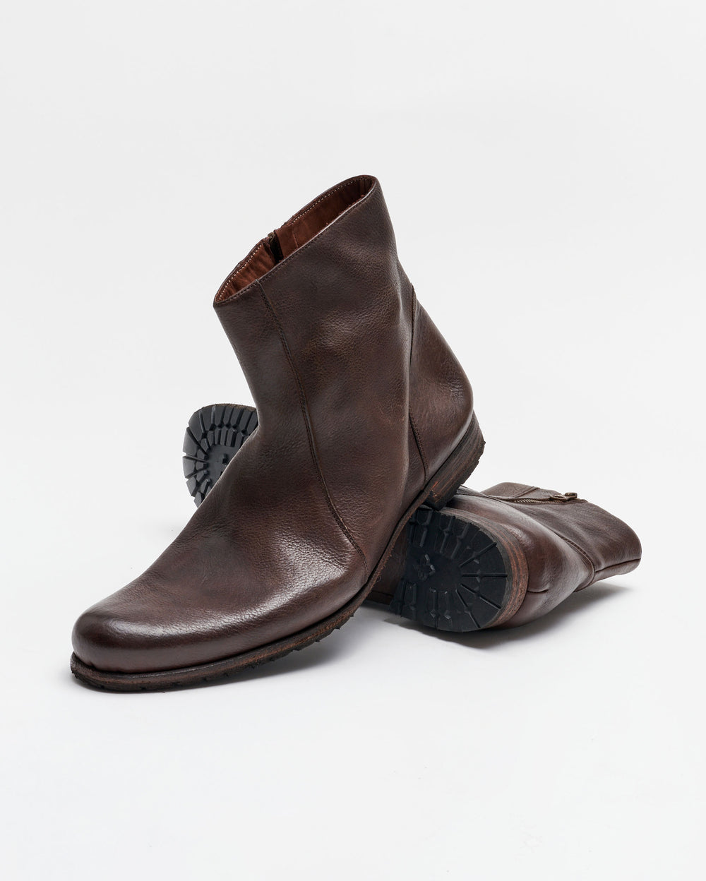 A pair of brown leather ankle boots with side zippers, one boot standing upright and the other lying on its side, showing the textured rubber sole. The background is plain white.