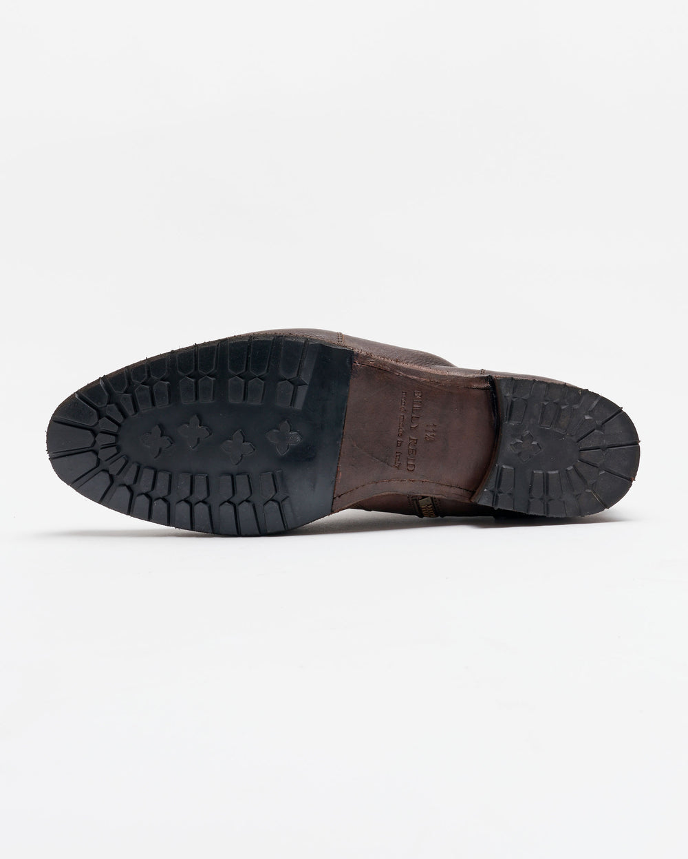 A brown leather shoe lying on its side, showing the black rubber sole with a rugged tread pattern, against a plain white background.