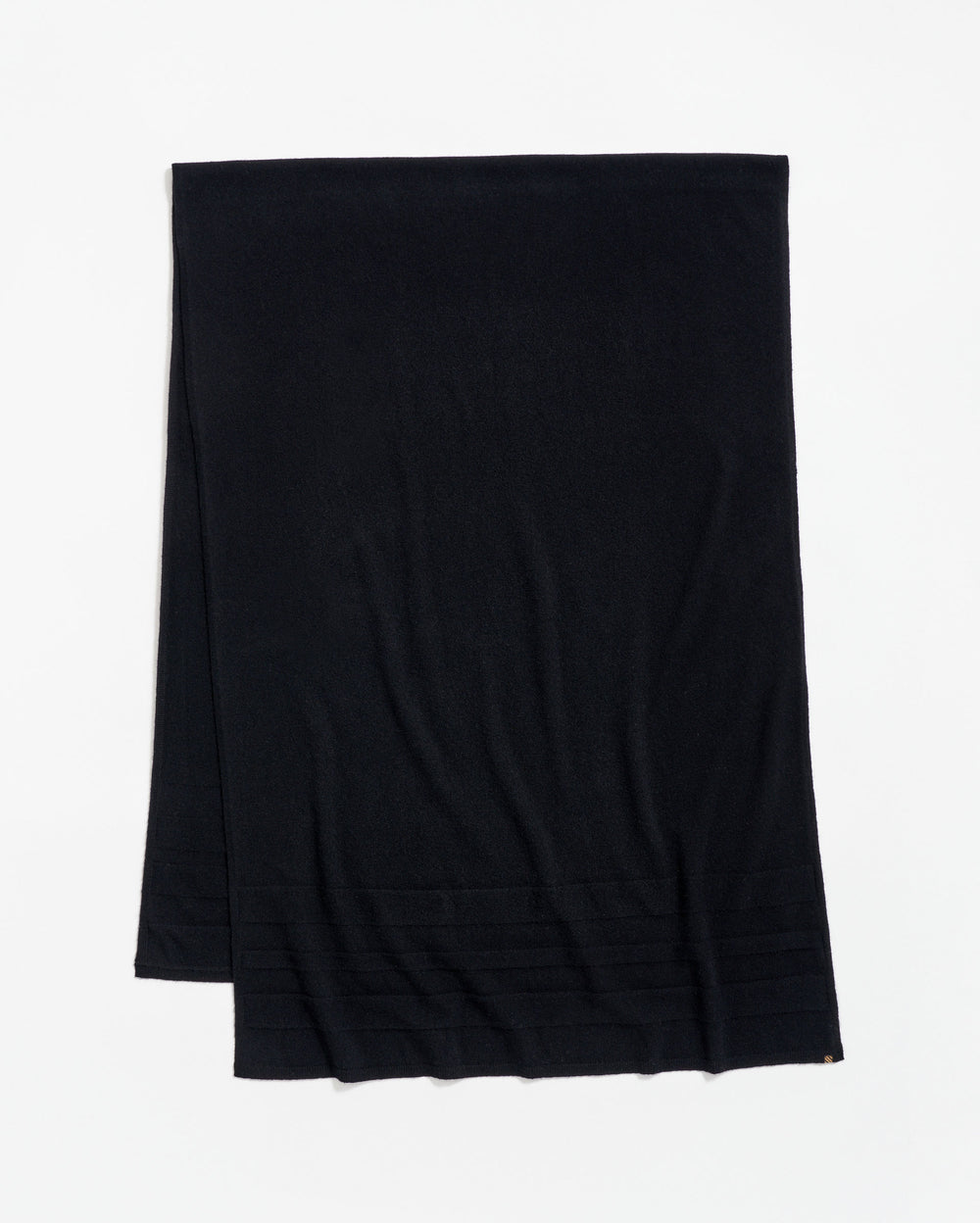 A plain black scarf is laid flat on a white surface, with a subtle ribbed pattern near one end.