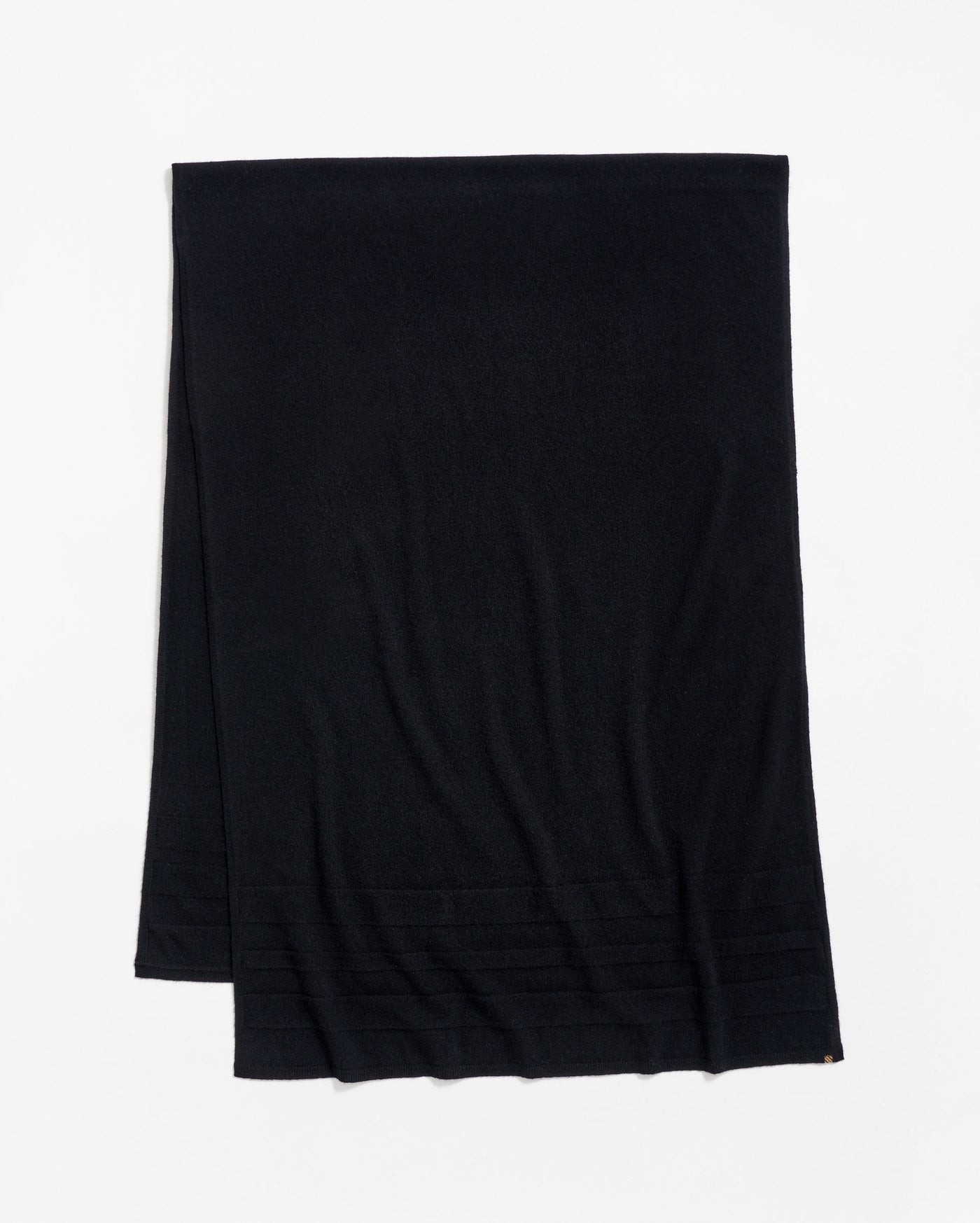 A plain black scarf is laid flat on a white surface, with a subtle ribbed pattern near one end.