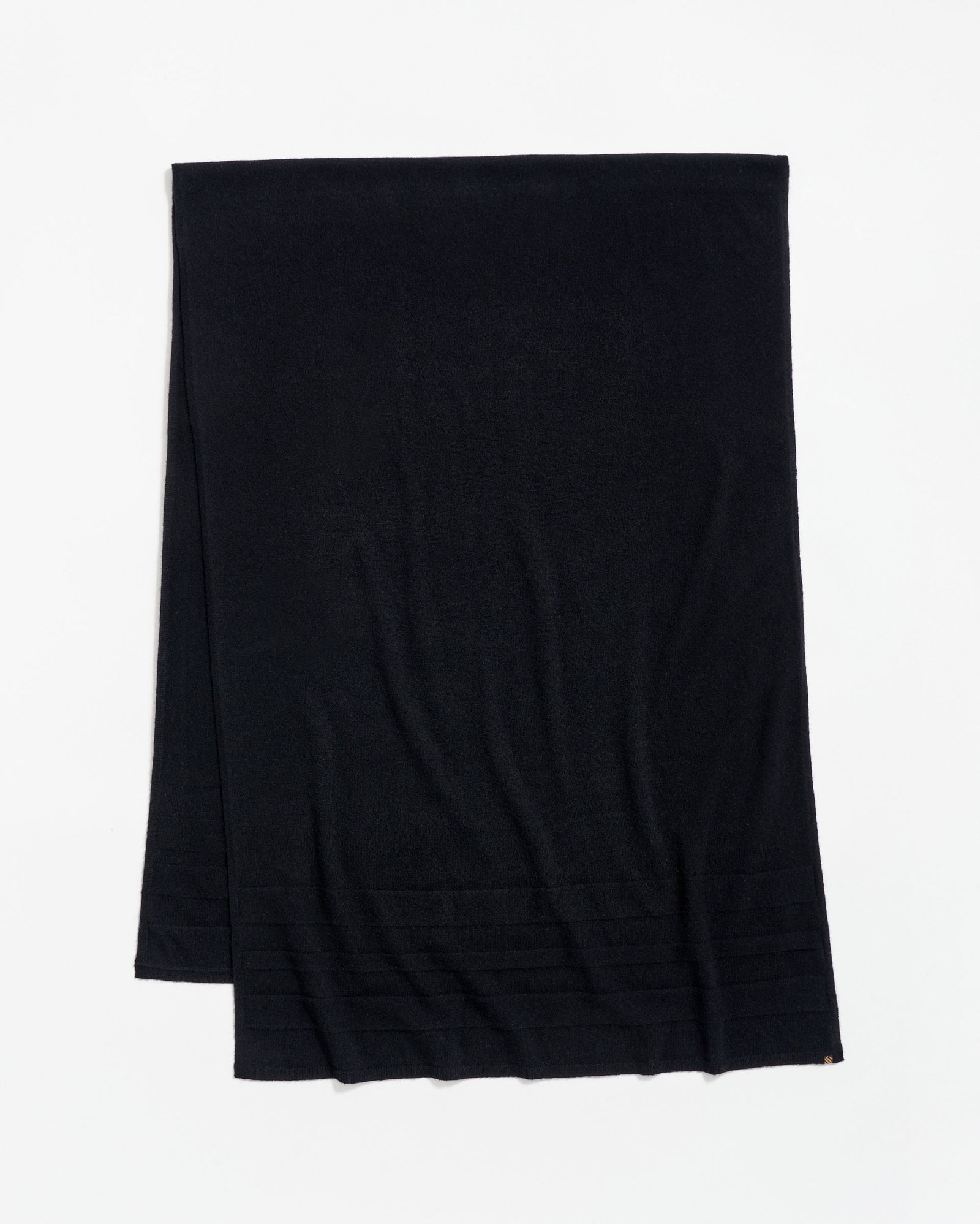A plain black scarf is laid flat on a white surface, with a subtle ribbed pattern near one end.