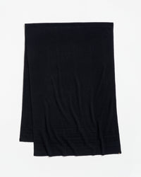 A plain black scarf is laid flat on a white surface, with a subtle ribbed pattern near one end.