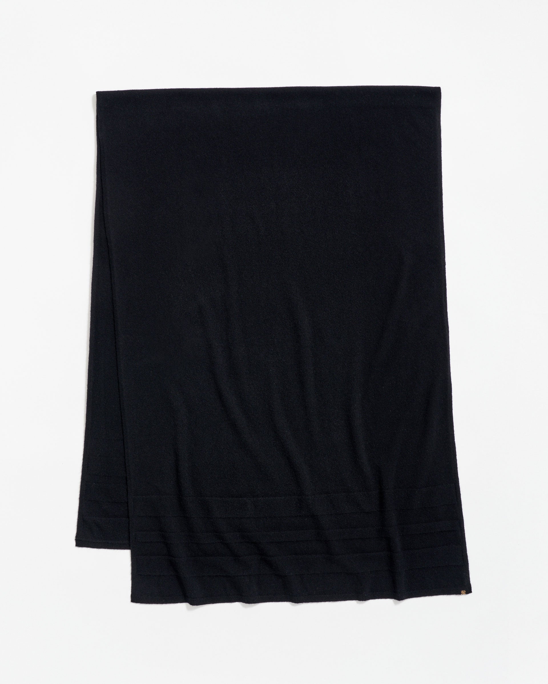 A plain black scarf is laid flat on a white surface, with a subtle ribbed pattern near one end.
