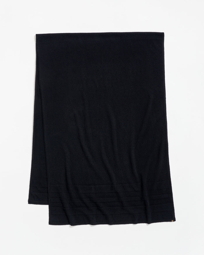 A plain black scarf is laid flat on a white surface, with a subtle ribbed pattern near one end.