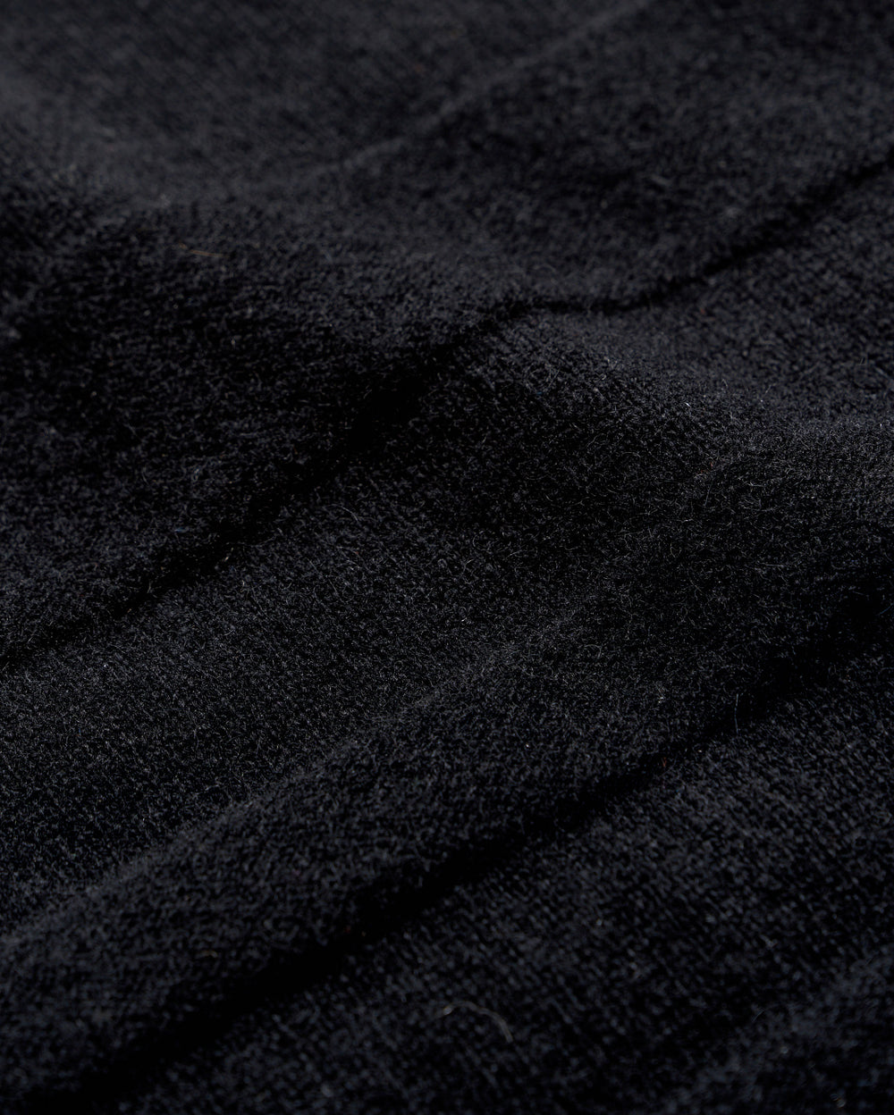 Close-up of black textured fabric with visible soft fibers and gentle folds, creating subtle shadows and depth across the surface.