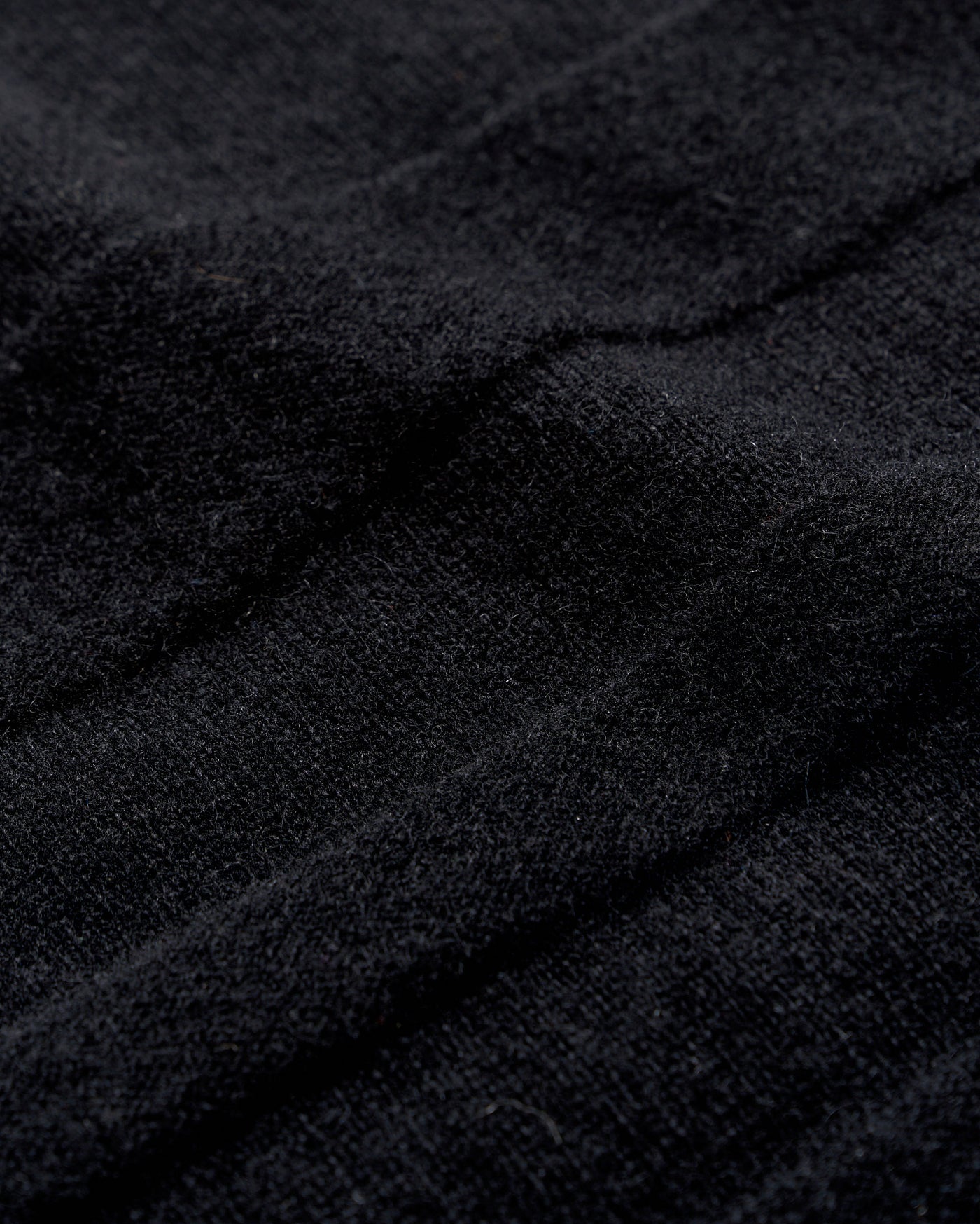 Close-up of black textured fabric with visible soft fibers and gentle folds, creating subtle shadows and depth across the surface.