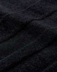 Close-up of black textured fabric with visible soft fibers and gentle folds, creating subtle shadows and depth across the surface.