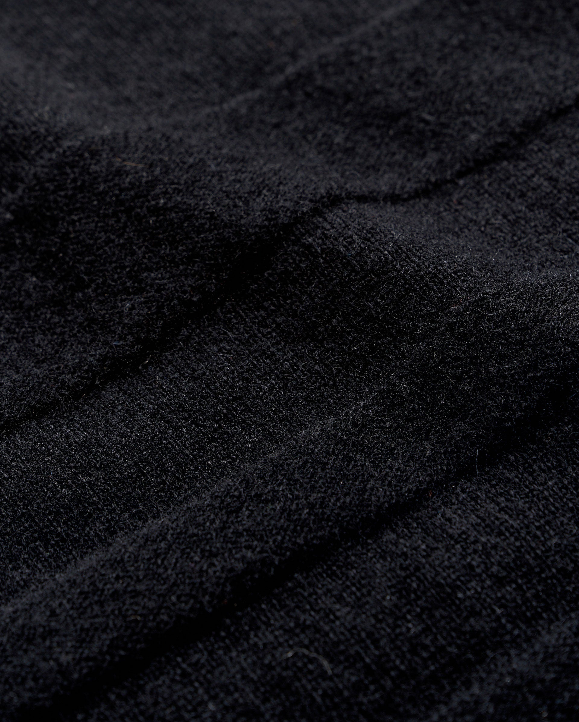 Close-up of black textured fabric with visible soft fibers and gentle folds, creating subtle shadows and depth across the surface.