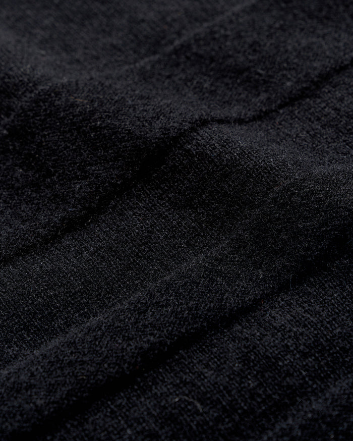 Close-up of black textured fabric with visible soft fibers and gentle folds, creating subtle shadows and depth across the surface.