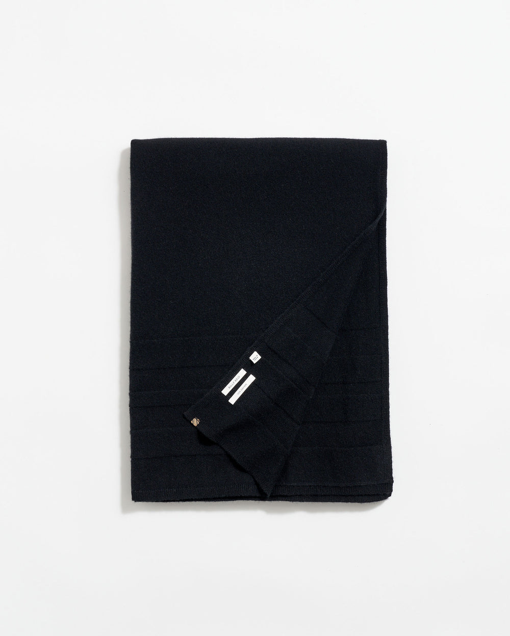 A neatly folded black scarf with subtle horizontal lines and a small section showing three white stripes near the corner, displayed on a plain white background.