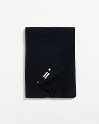 A neatly folded black scarf with subtle horizontal lines and a small section showing three white stripes near the corner, displayed on a plain white background.