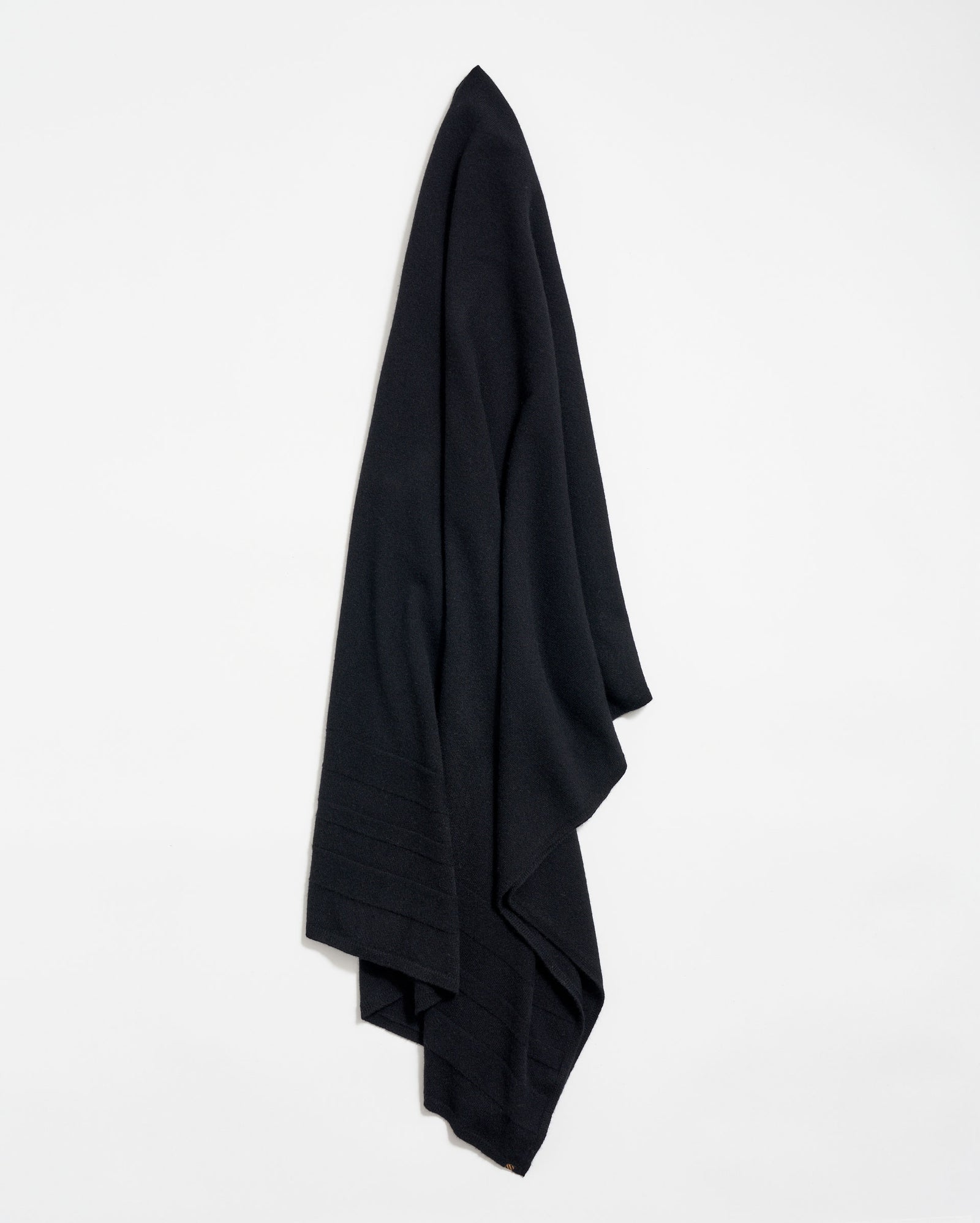 A large, black fabric cloth hangs neatly against a plain white wall, draped in soft folds.