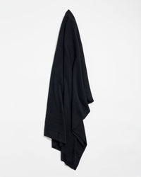 A large, black fabric cloth hangs neatly against a plain white wall, draped in soft folds.