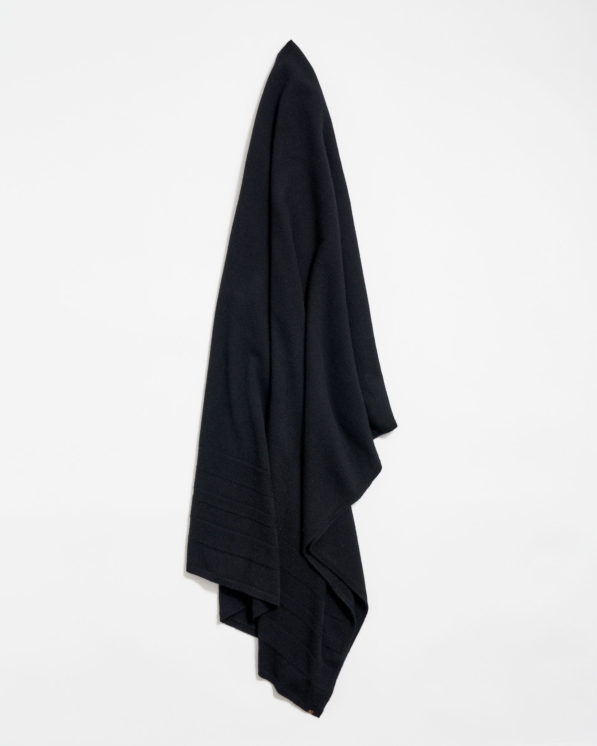 A large, black fabric cloth hangs neatly against a plain white wall, draped in soft folds.