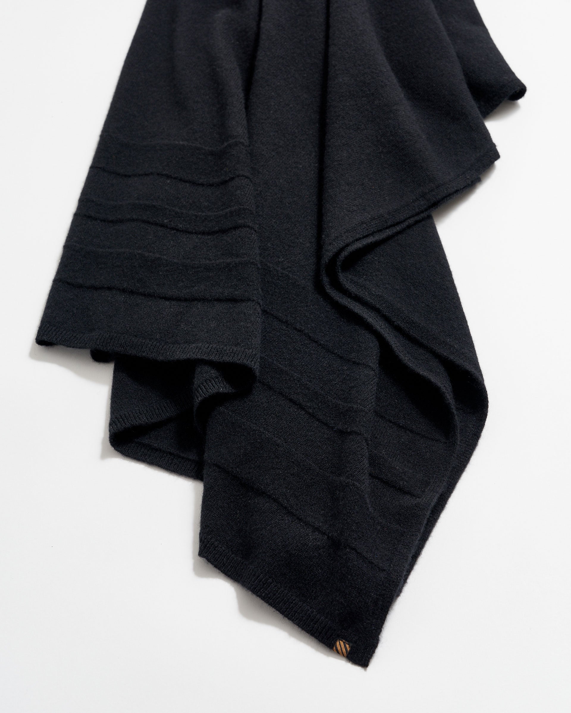 A folded black wool scarf with subtle horizontal ribbed lines, displayed on a white background.