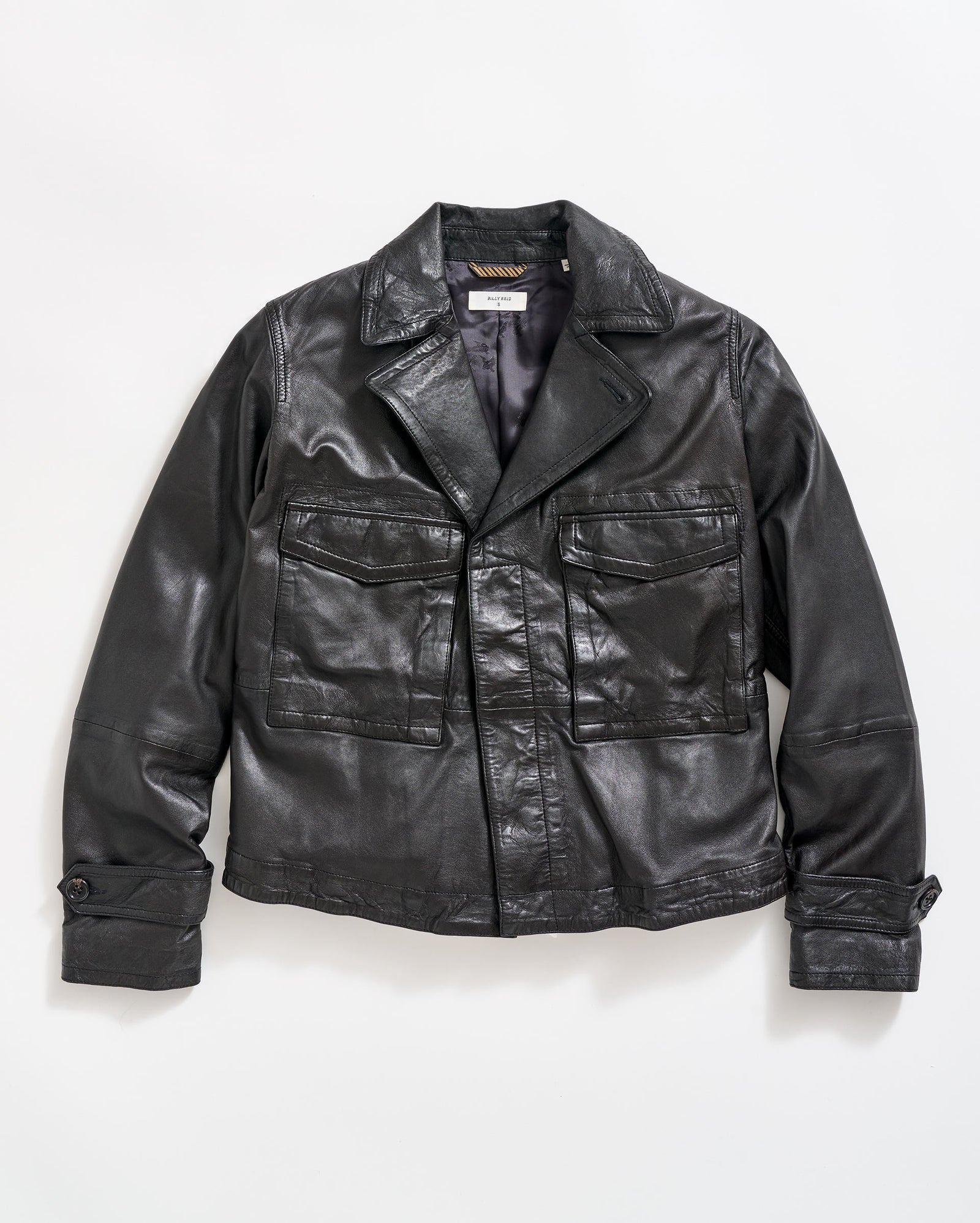 A black leather jacket with large front pockets, buttoned cuffs, and a notched collar, laid flat on a white background.