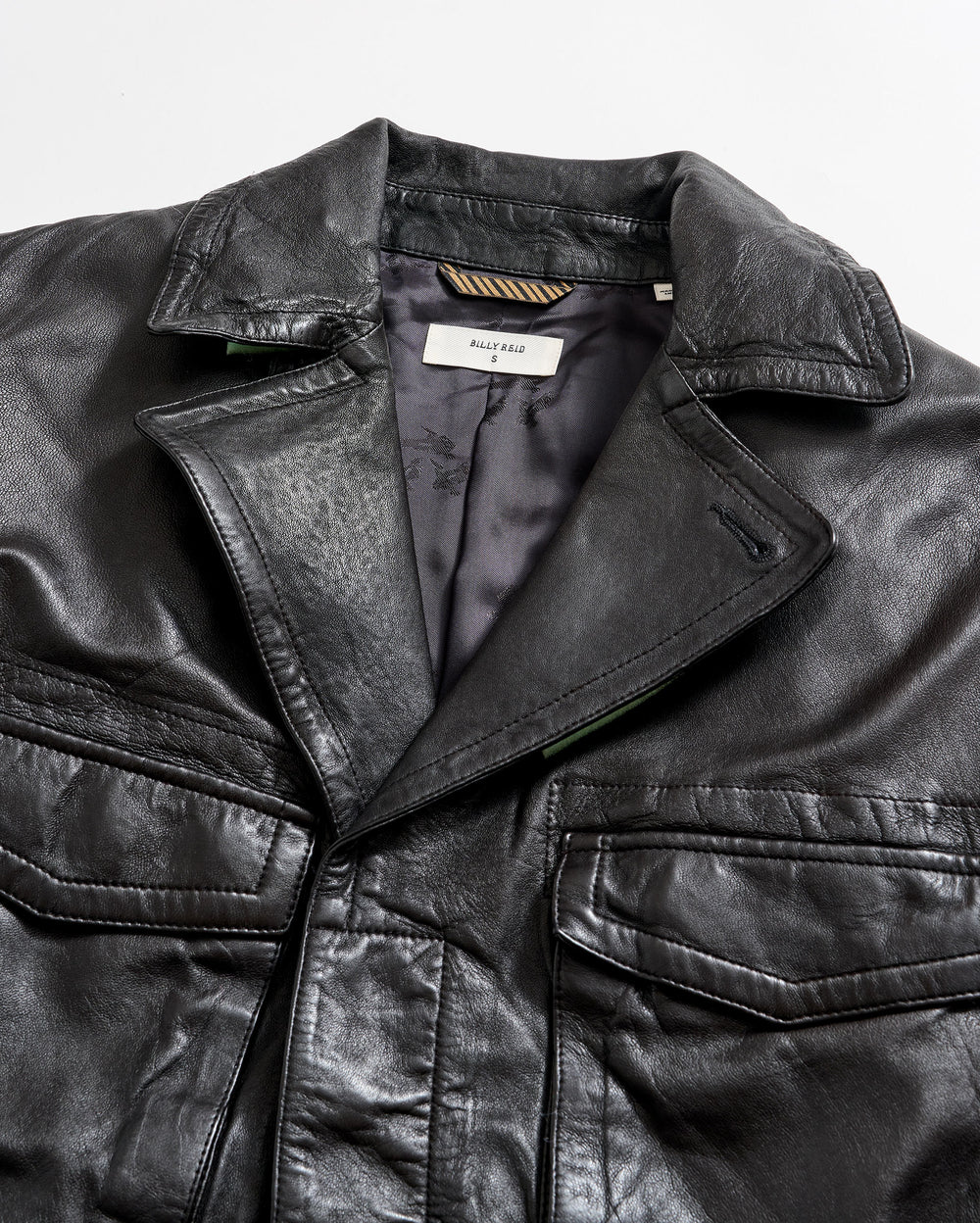 A close-up of a black leather jacket with a visible collar, front pockets, and a partially open front showing a tag labeled “BALLY KEAL” on the inside lining.
