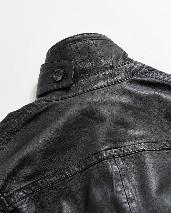 Close-up of the upper back and collar of a black leather jacket with visible stitching and a buttoned strap detail on the collar, set against a plain white background.