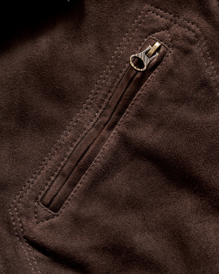 Close-up of a brown suede fabric featuring a zippered pocket with visible stitching and a metallic zipper pull.