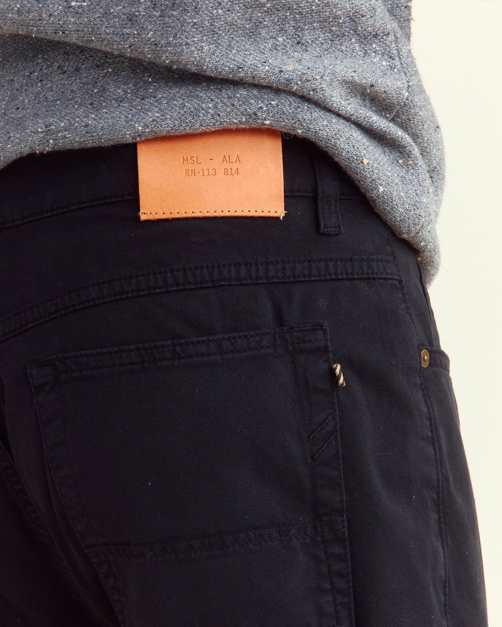 A close-up of a person wearing black pants and a gray shirt, with a brown leather patch above the back pocket that reads MSL - ALA RN-113 814.