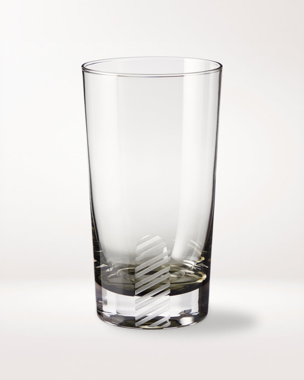 A clear empty glass tumbler with a vertical, diagonal-striped frosted pattern near the base, placed on a plain white background.