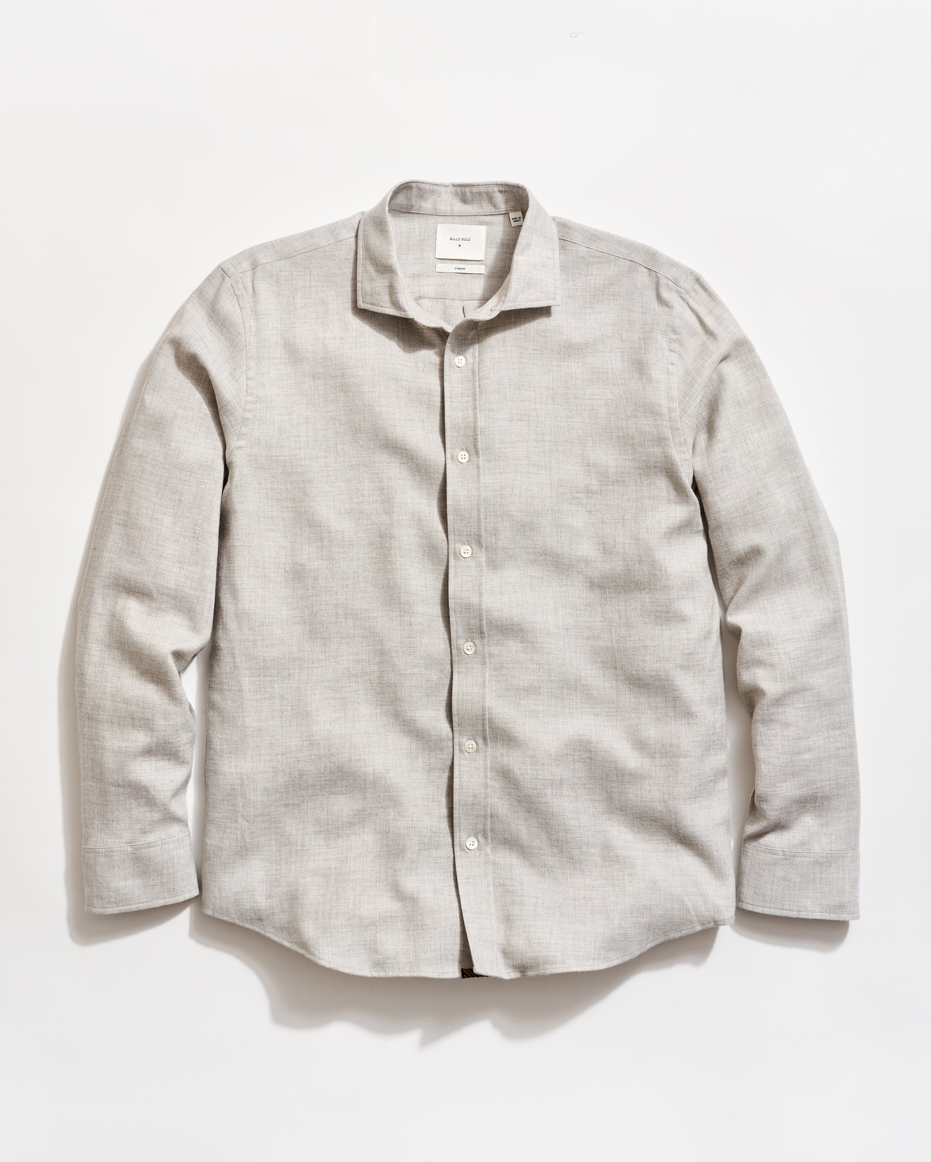 A light gray, long-sleeve button-up shirt with a collar, laid flat on a white background. The shirt has white buttons and a slightly textured fabric.