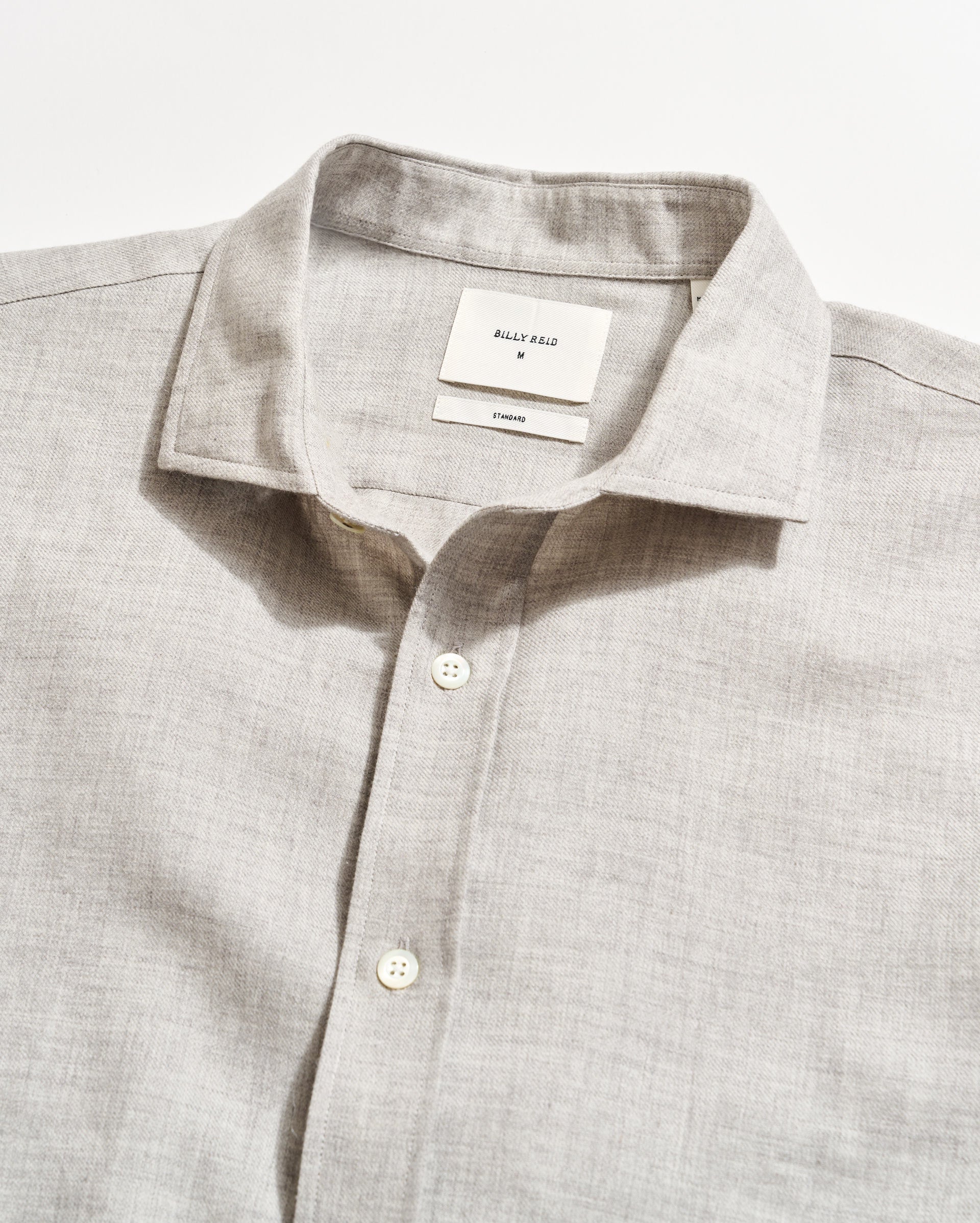 A light gray long-sleeve button-up shirt with a collar, neatly laid flat on a white surface. The shirt features white buttons and a visible inner tag labeled BILLY REID with size and care information.