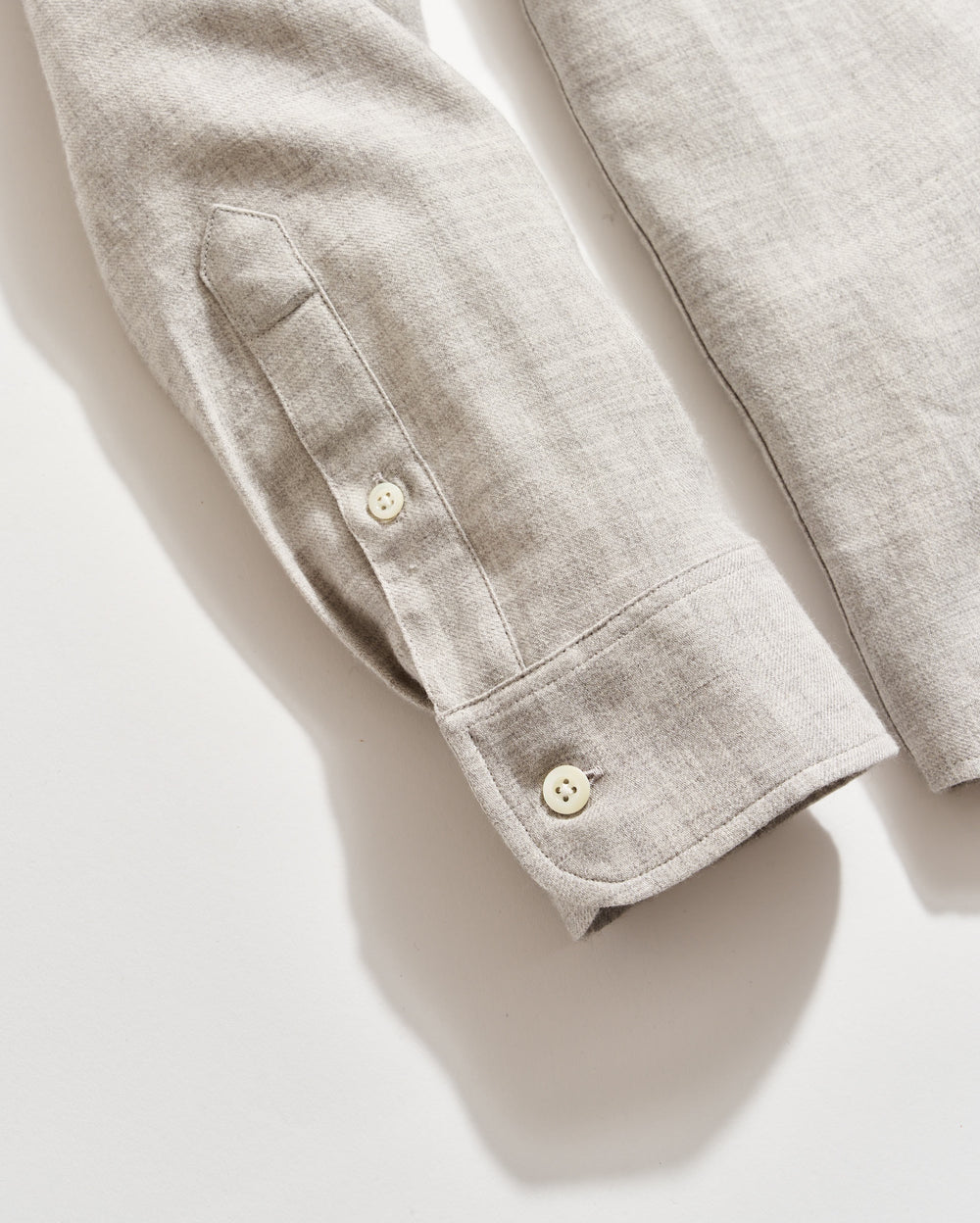 A close-up of a light beige long-sleeve shirt made of linen fabric, showing the cuff, sleeve placket, and two cream-colored buttons against a white background.