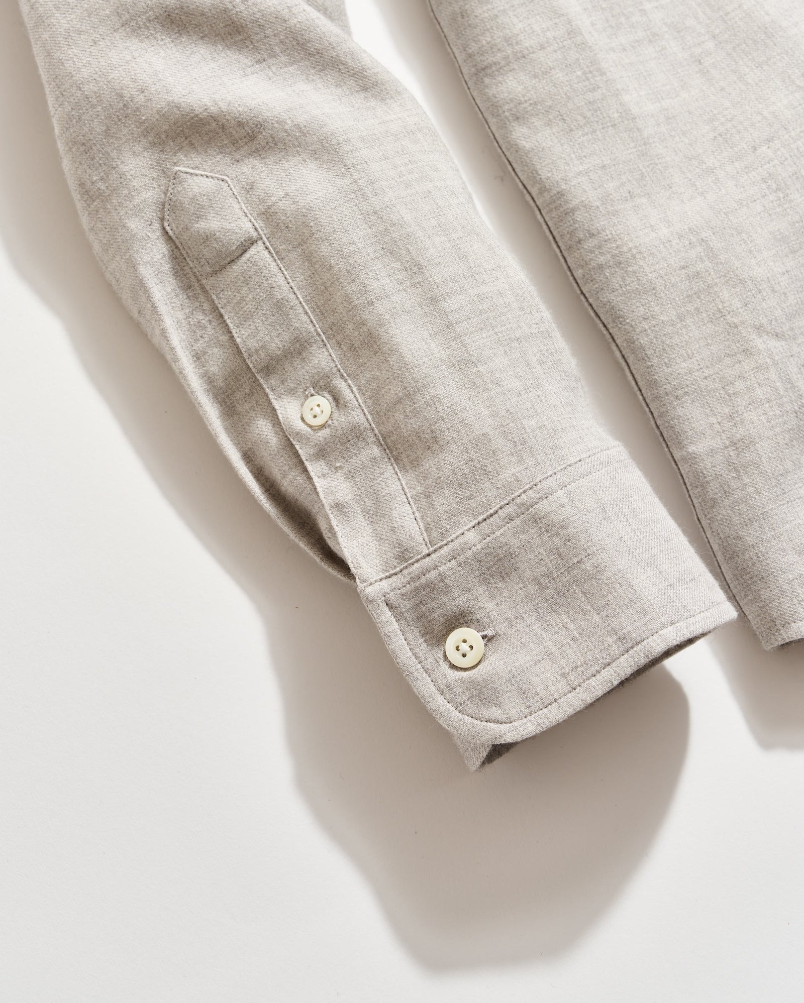 A close-up of a light beige long-sleeve shirt made of linen fabric, showing the cuff, sleeve placket, and two cream-colored buttons against a white background.