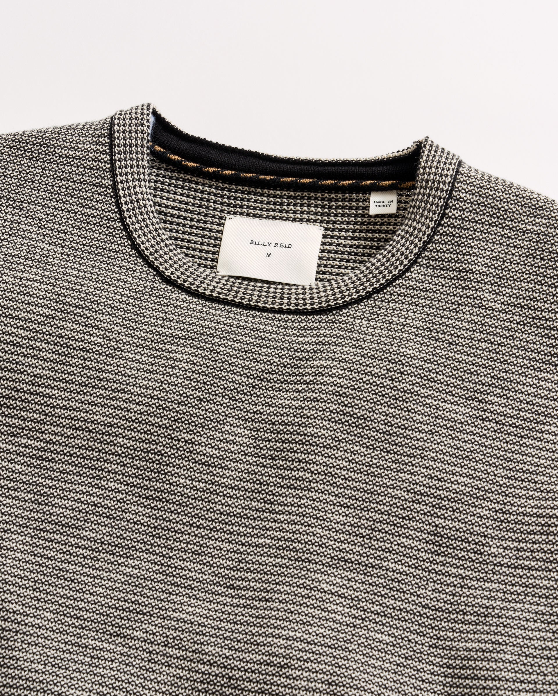 Close-up of a gray textured sweater with brand labels on a light gray background
