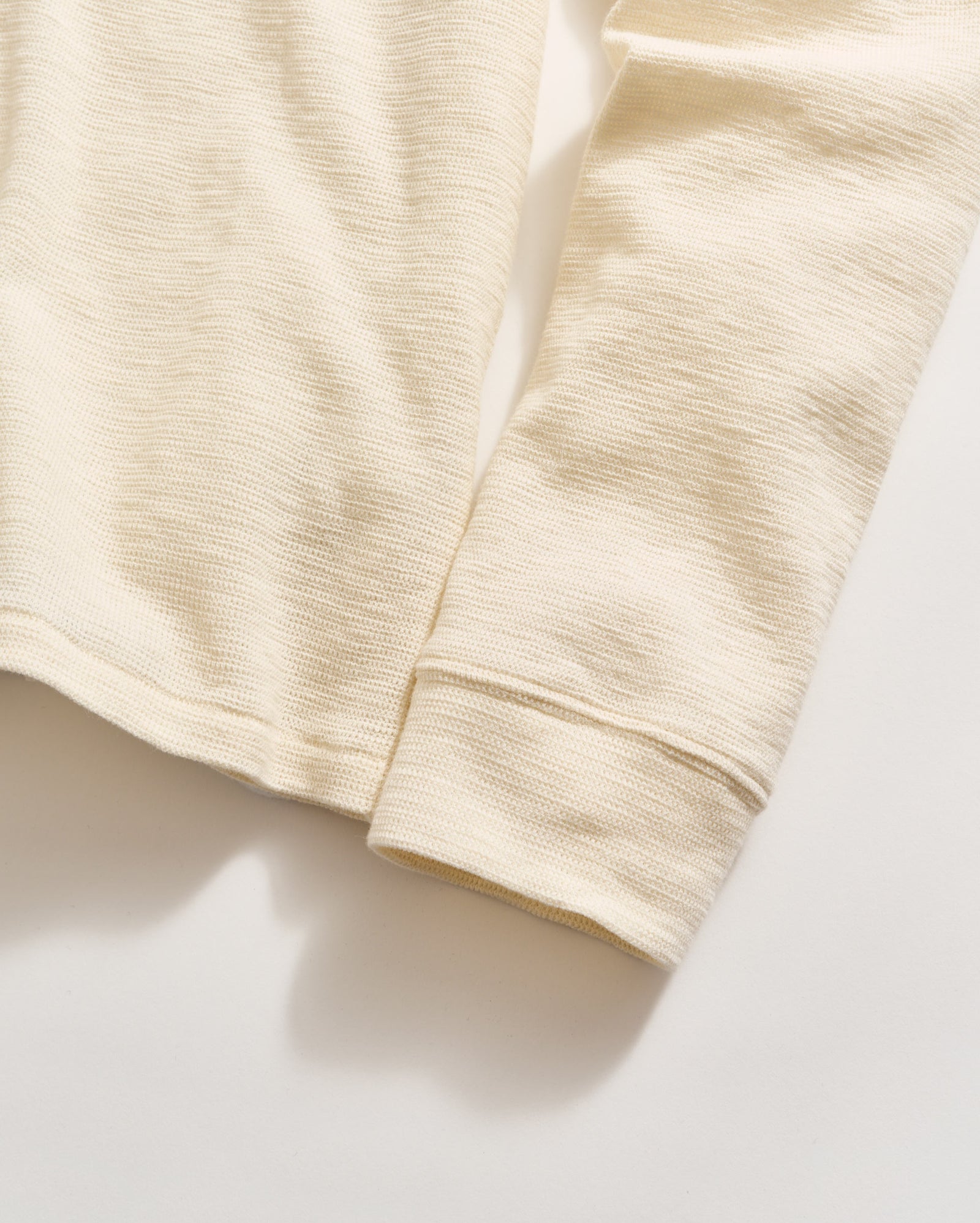 A close-up view of a long-sleeve cream-colored textured shirt, focusing on the sleeve and lower hem against a light background.
