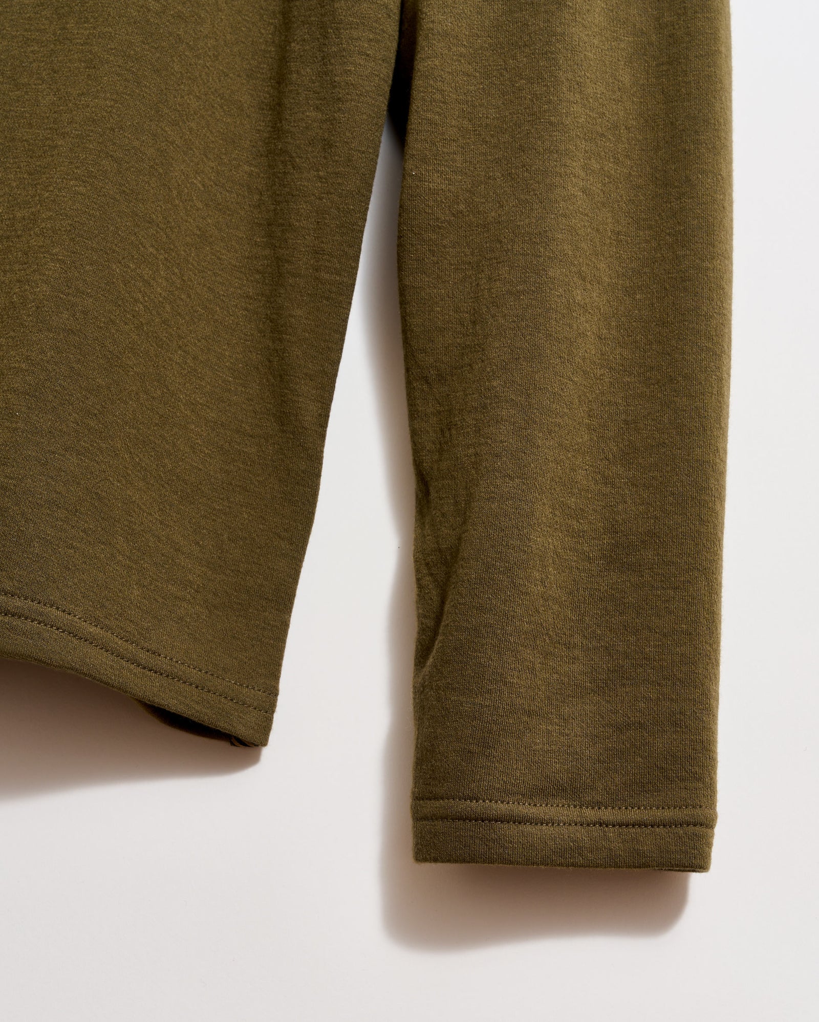 Close-up of the lower part of a long-sleeve olive green shirt, showing the hem and sleeve cuff against a light background.