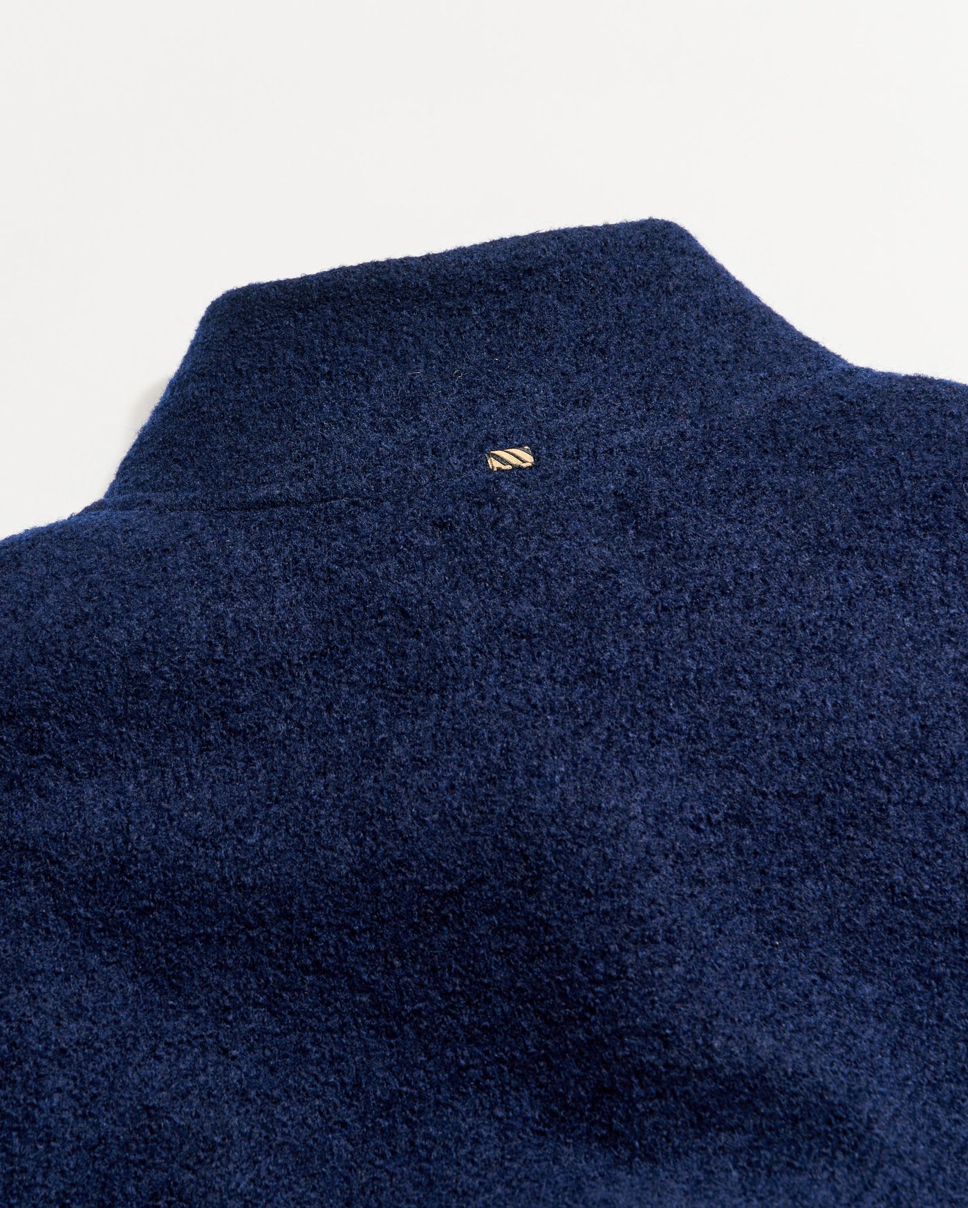 Close-up of the back of a textured navy blue fleece jacket with a small rectangular gold logo at the upper center below the collar.