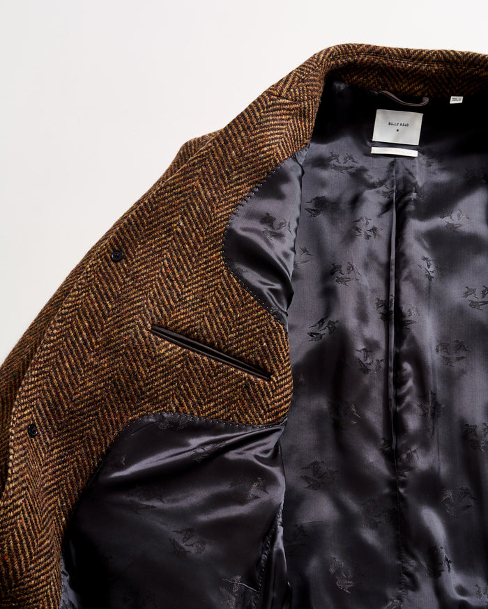 A close-up of a brown herringbone-patterned blazer, partially open to reveal a smooth, dark gray satin lining with subtle floral designs and a white label at the collar.