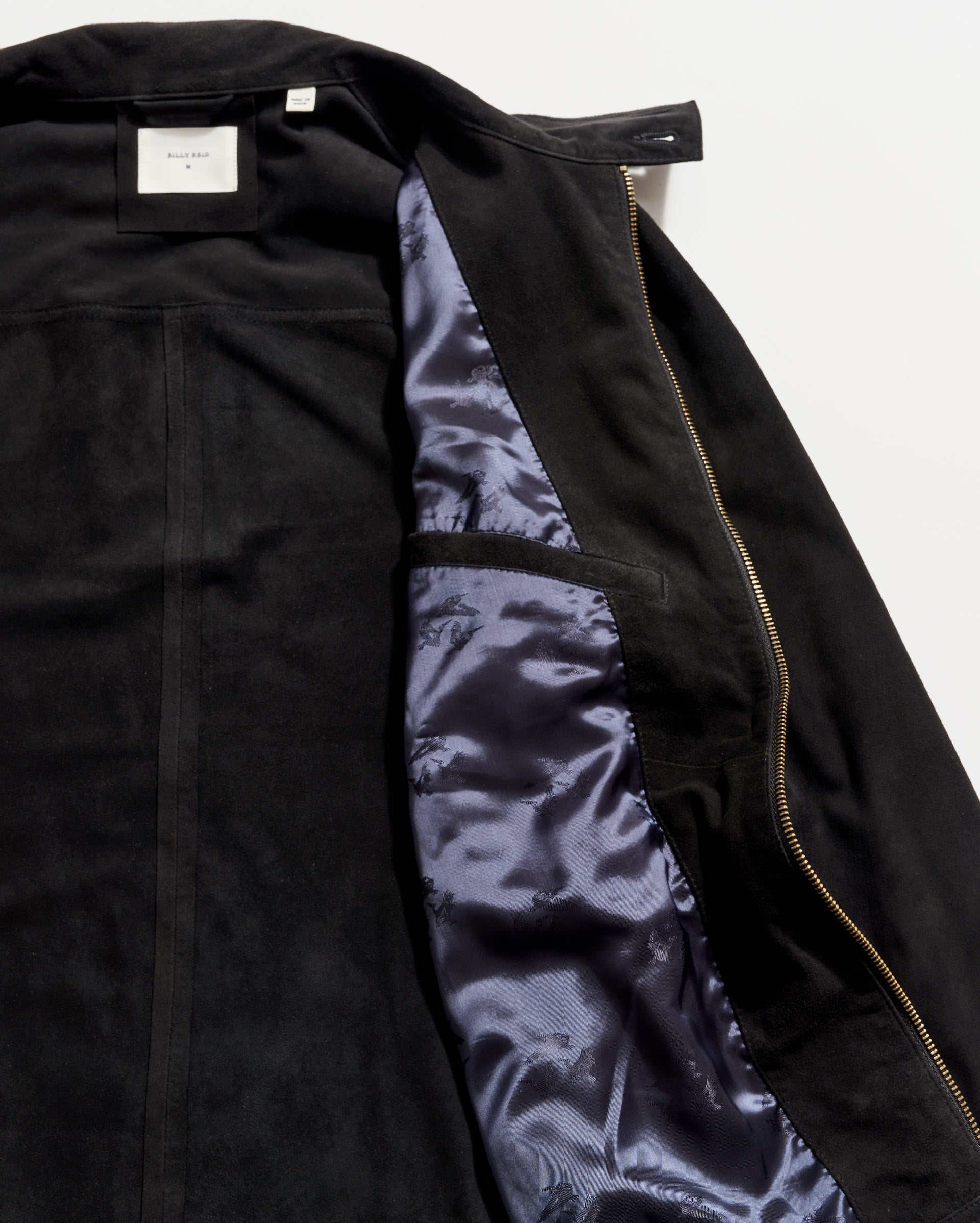 Black suede jacket partially unzipped to reveal a shiny dark blue satin lining and an interior pocket on the left side, with a white label visible at the collar.