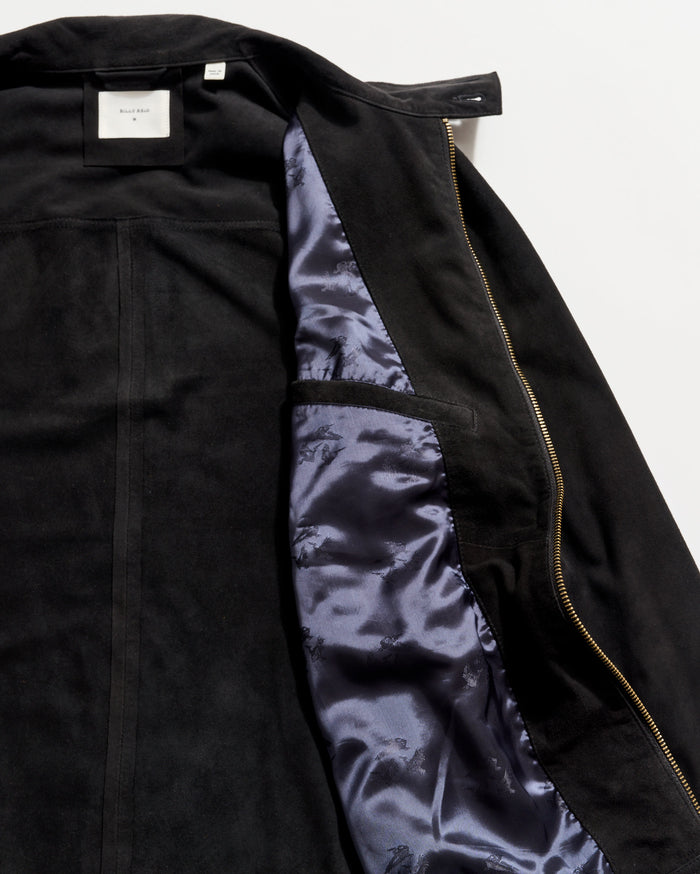 Black suede jacket partially unzipped to reveal a shiny dark blue satin lining and an interior pocket on the left side, with a white label visible at the collar.