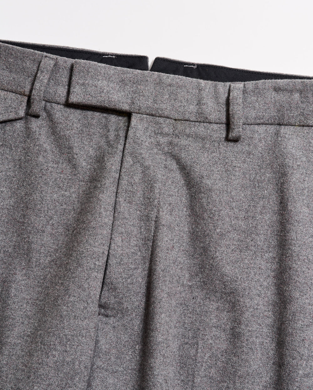 Close-up of the waistband and upper section of a pair of grey dress trousers, showing belt loops, pleats, and part of the zipper area against a plain background.
